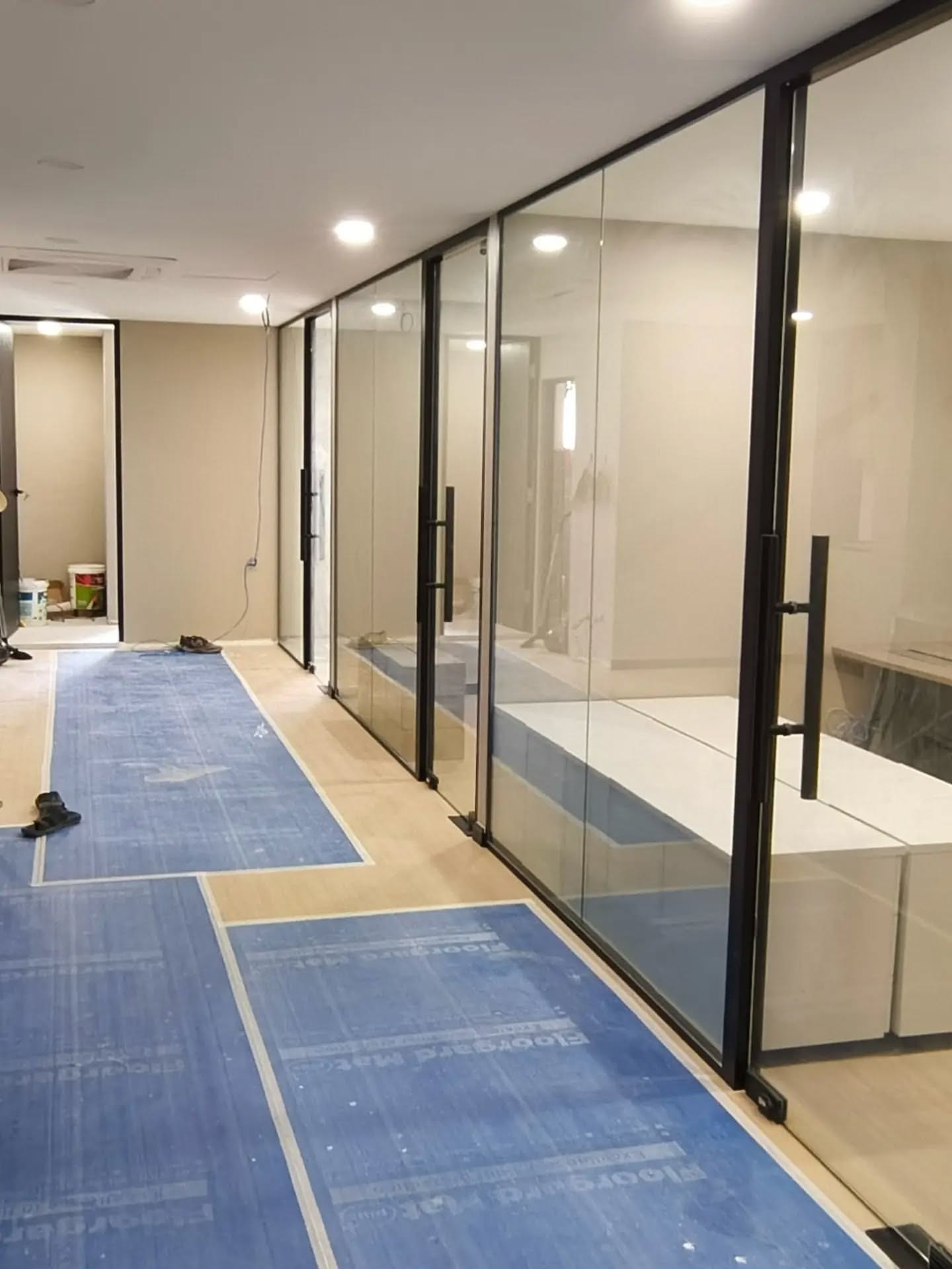 A corridor lined with black-framed glass partitions, the floor still covered with protective sheeting.