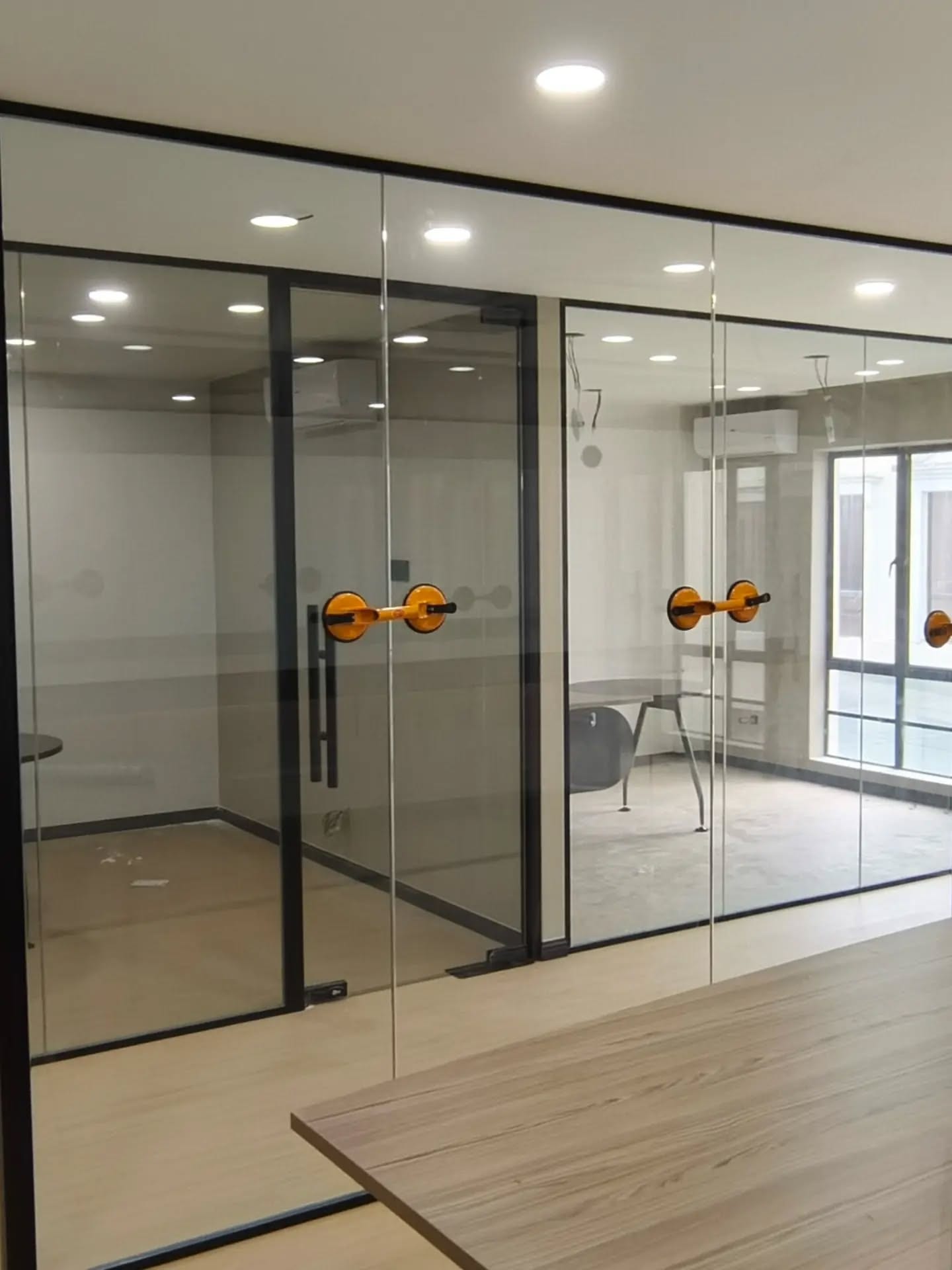 Black-framed double glass doors with long vertical pull handles, set into a glazed partition run.