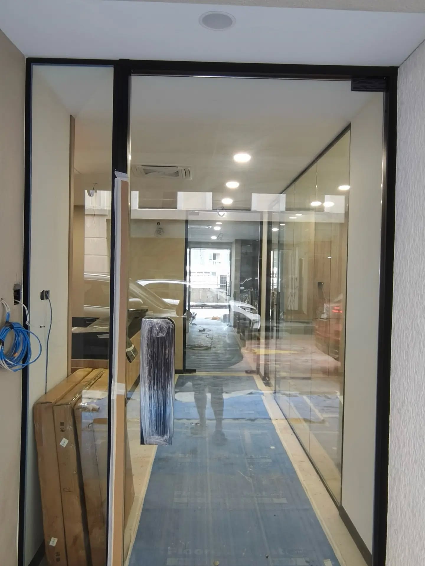 A frameless glass wall and glass door installed on a bare concrete screed floor, with the ceiling services already in place.