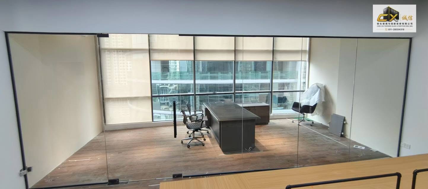A black-framed glass partition forming a manager's room against a full-height window wall with roller blinds.
