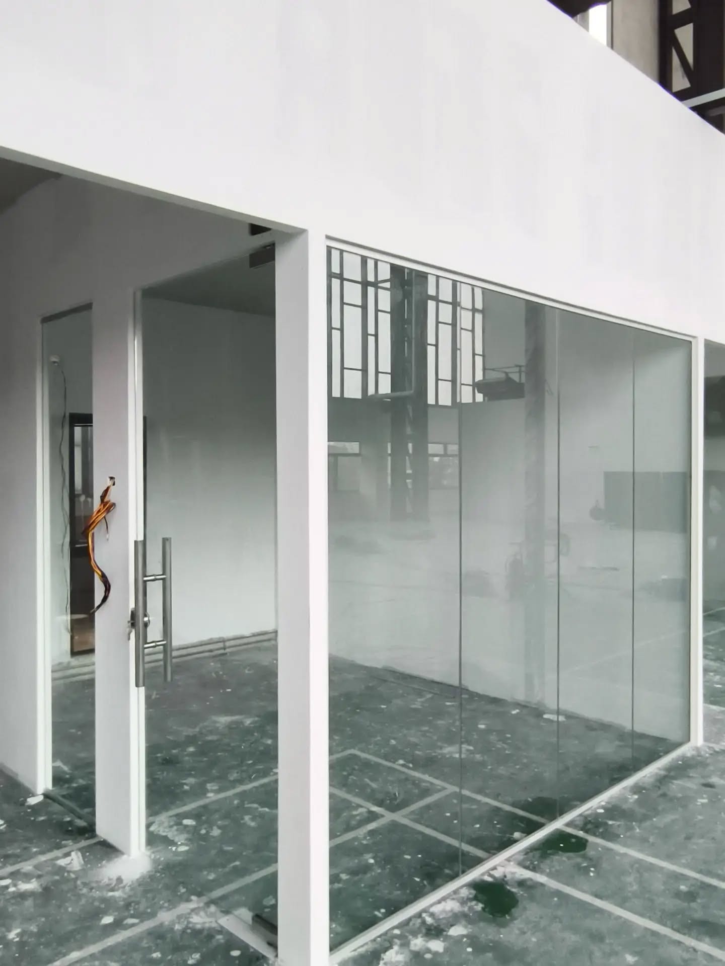 A frameless tempered-glass room with a timber desk and a round table inside.