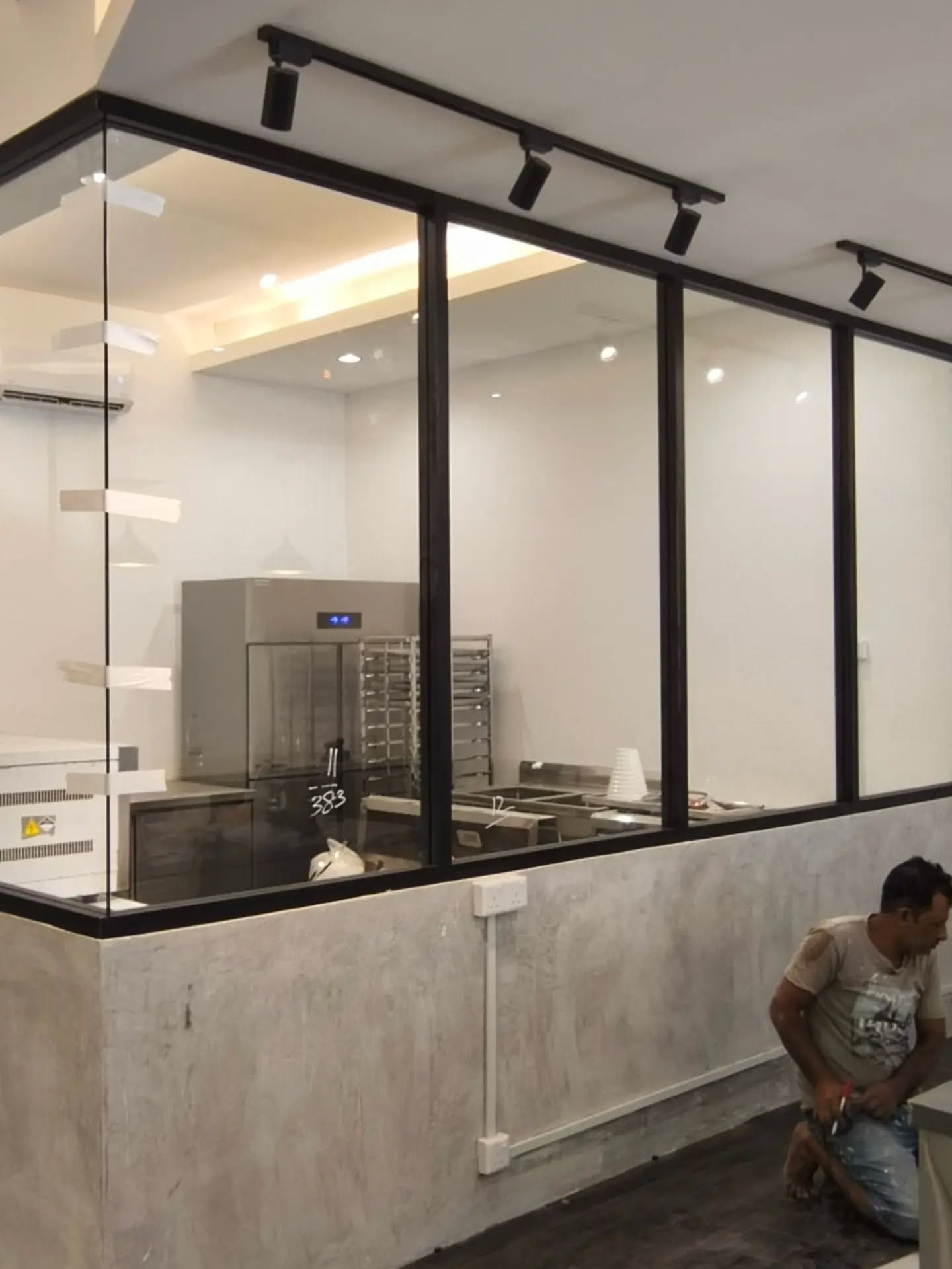Two installers fitting a black-framed glazed screen above a service counter.