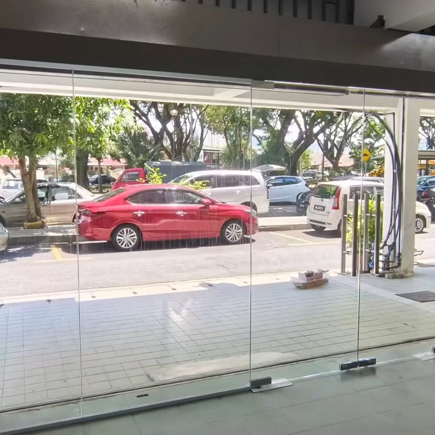 A frameless glass shop entrance seen from inside, with the street and parked cars beyond.