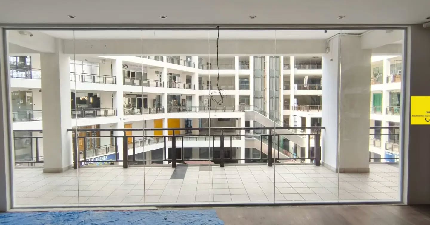 A full-height frameless glass shopfront looking out over a shopping-mall atrium.